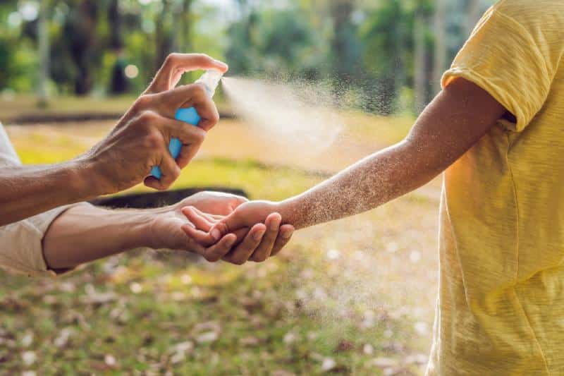 woman spray mosquito repellent on child's arm