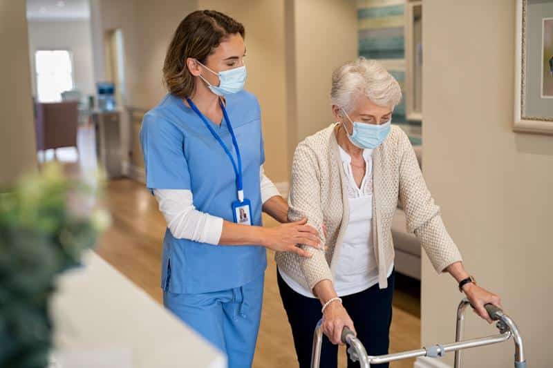 nurse helping senior citizen walk with a walker down a hall