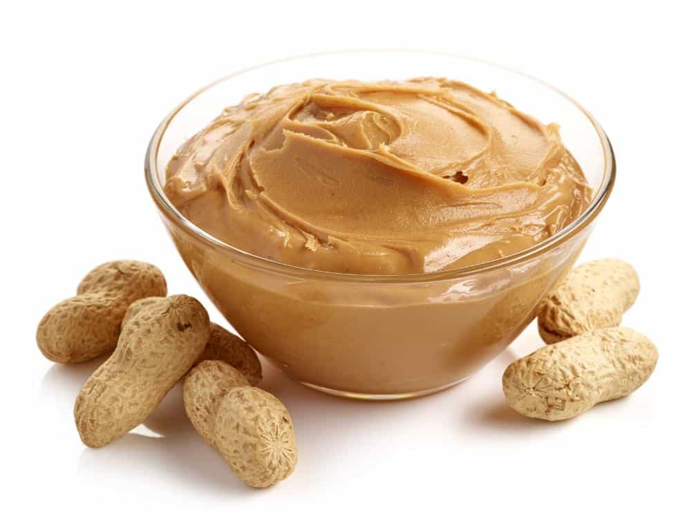 bowl of creamy peanut butter with whole peanuts in their shells isolated on a white background