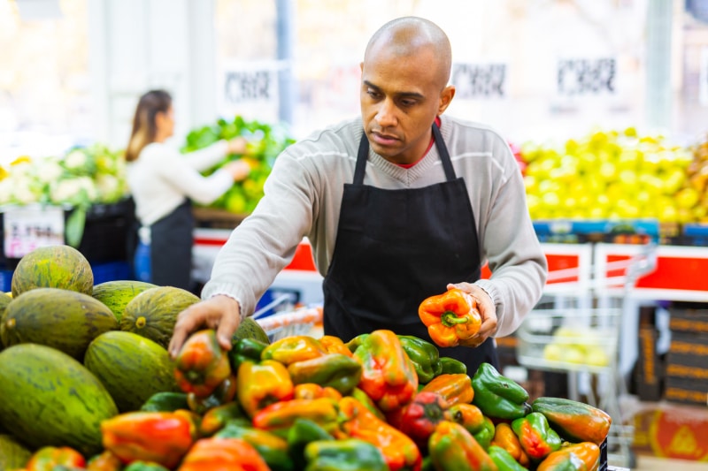 Supermarket employee in apron checking products in vegetable department