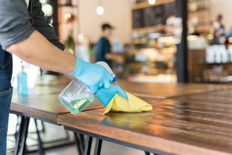 Waiter cleaning table with disinfectant spray and Microfiber cloth in cafe