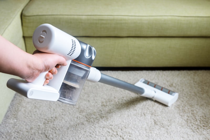 Person using a cordless bagless vacuum to vacuum carpet in living room