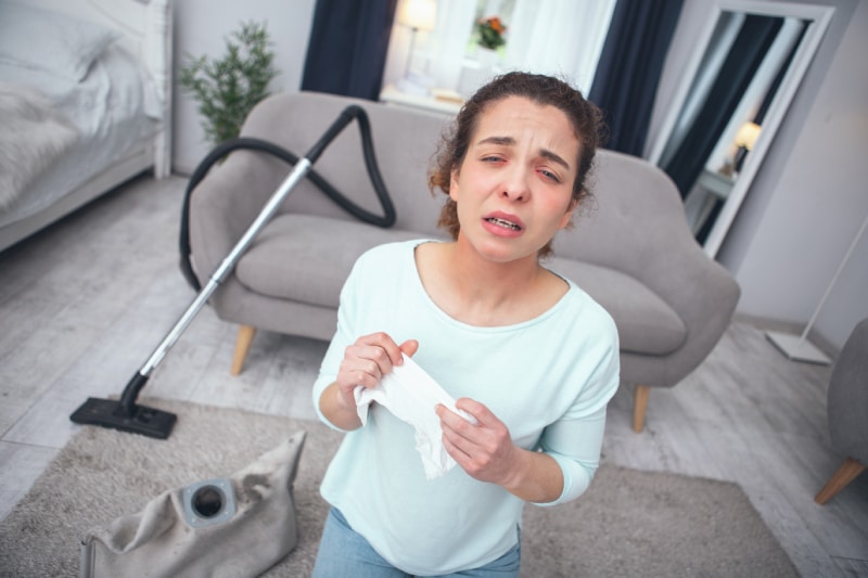 woman sneezing while cleaning her living room with a vacuum 